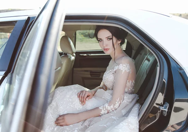 时尚照片的美丽新娘与深色的头发在优雅的婚纱礼服 摆在车上 — 图库照片
