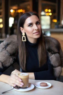 kafede otururken lüks kürk ceket siyah saçlı güzel kadın tatlı ile kahve içmek moda açık fotoğrafı