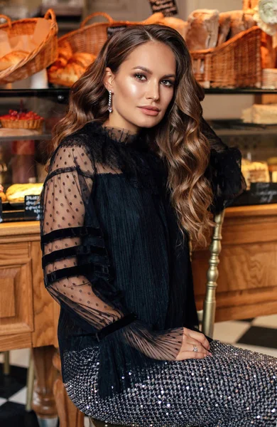 时尚内饰照片美丽的女人与黑头发在优雅的礼服摆姿势在优雅的面包店咖啡馆 — 图库照片