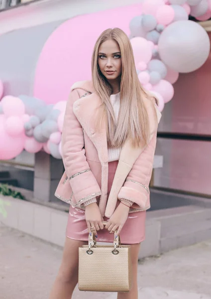 fashion street look of beautiful young woman with long blond hair in elegant clothes walking by the street