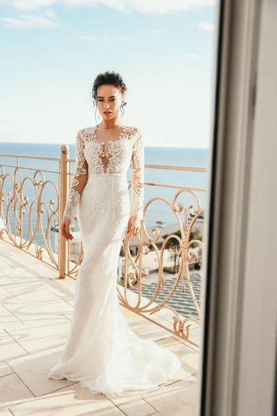 时尚照片美丽的女人新娘与黑头发在豪华的婚纱礼服摆姿势在阳台上与海景 — 图库照片