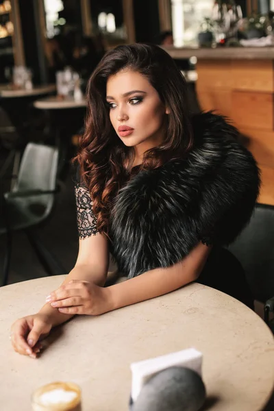 カフェに座っているエレガントなドレスに黒い髪を持つ美しい若い女性のファッション写真 テーブルの上のカプチーノのカップ — ストック写真