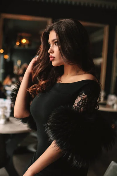 时尚照片美丽的年轻女子与黑头发在优雅的礼服坐在咖啡馆 — 图库照片