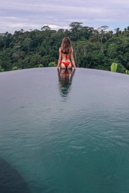 Koyu saçlı, kırmızı bikinili, kenarlarda poz veren güzel bir kadın. 