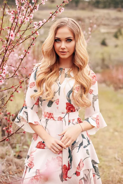 Beautiful girl  with blond hair in elegant dress posing among fl — Stock Photo, Image