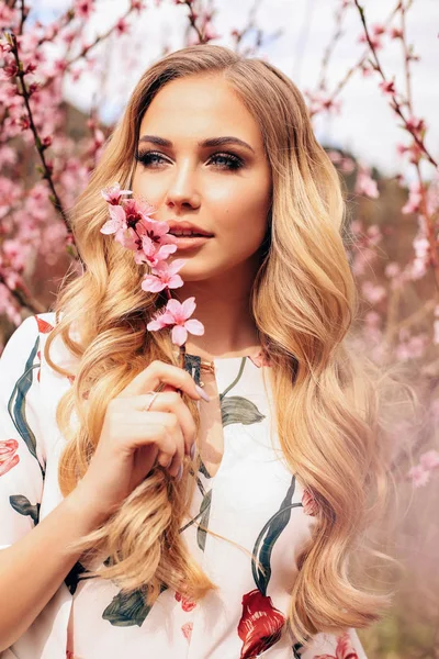 Hermosa chica con el pelo rubio en vestido elegante posando entre fl — Foto de Stock