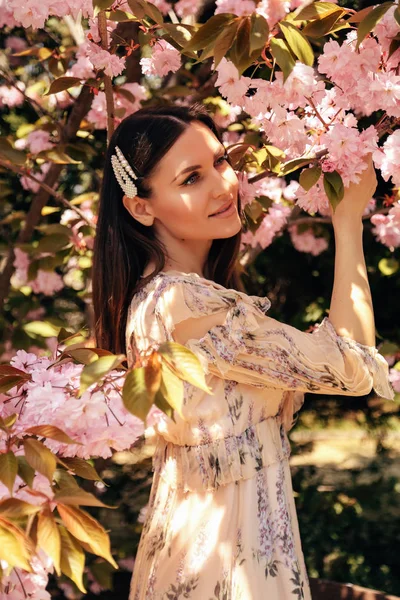 Woman with dark hair in elegant dress posing near flowering saku — Stock Photo, Image