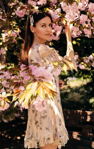 Woman with dark hair in elegant dress posing near flowering saku — Stock Photo, Image