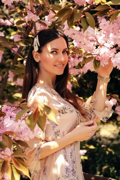 Woman with dark hair in elegant dress posing near flowering saku — Stock Photo, Image