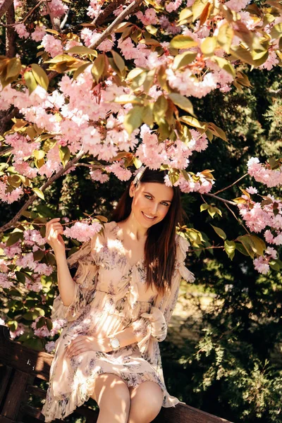 Woman with dark hair in elegant dress posing near flowering saku — Stock Photo, Image