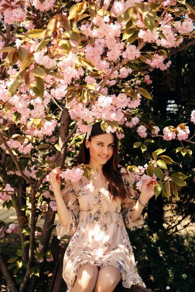 Woman with dark hair in elegant dress posing near flowering saku — Stock Photo, Image