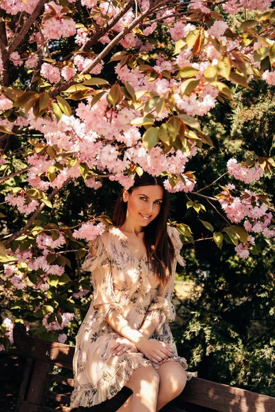 Woman with dark hair in elegant dress posing near flowering saku — Stock Photo, Image