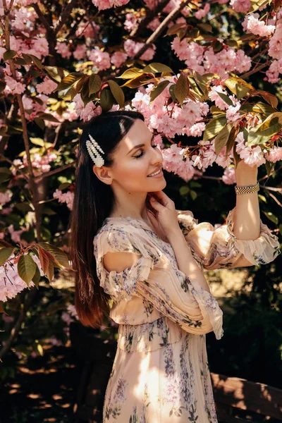 Vrouw met donker haar in elegante jurk poseren in de buurt van bloeiende saku — Stockfoto