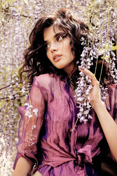 时尚的户外照片 美丽的性感女人 深色头发 华丽的衣服和饰物 躺在花园里 长着盛开的紫藤树 — 图库照片