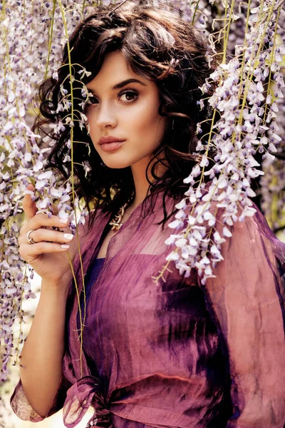 美しい官能的な女性のファッション屋外写真豪華な服やアクセサリーで暗い髪藤の木が咲く庭にポーズをとって — ストック写真