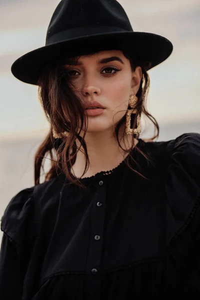 エレガントな服に黒い髪をした美しい女性のファッション屋外写真やビーチでポーズをとる黒い帽子 — ストック写真