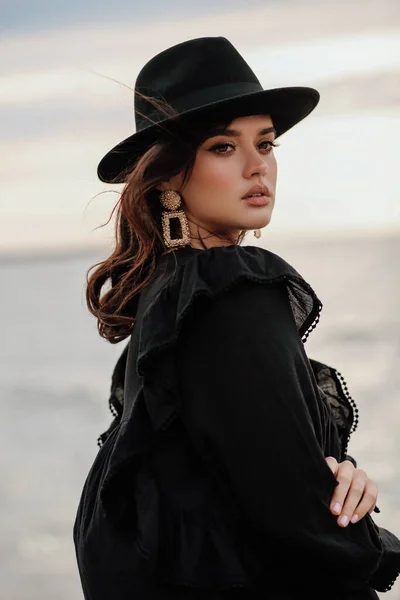 エレガントな服に黒い髪をした美しい女性のファッション屋外写真やビーチでポーズをとる黒い帽子 — ストック写真