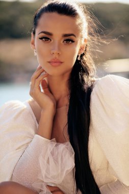 Güzel, siyah saçlı, lüks beyaz elbiseli, güzel manzaralı, deniz manzaralı güzel bir kadının moda fotoğrafı.