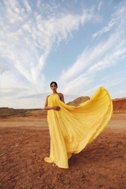 Güzel, siyah saçlı, şık elbiseli ve aksesuarlı, çölde poz veren seksi bir kadının moda fotoğrafı.