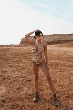Güzel, siyah saçlı, şık mayo giymiş ve çöl ortasında poz veren güzel bir kadının moda fotoğrafı.
