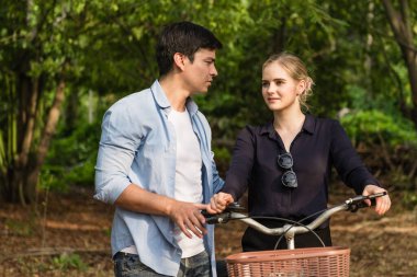 Mutlu genç çift aşık ve güneşli bir günde parkta bisiklet sürmeye gidiyorlar..