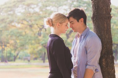 Birbirine aşık genç bir çift, parkta ağacın altında sarılıyorlar.