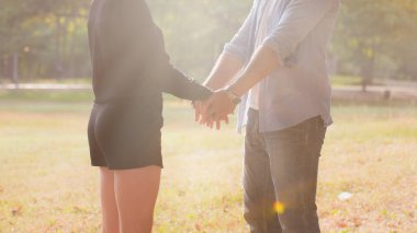 Birbirine aşık genç bir çift sonbahar parkında el ele tutuşup gün batımına bakıyor.