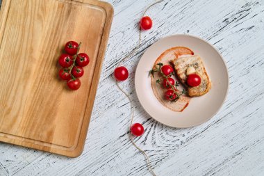 Domuz eti, ızgara ve beyaz ahşap masada vişneli domatesle servis edilir.