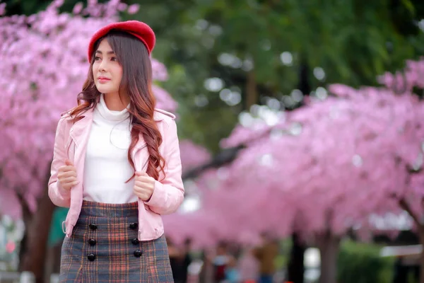 春の日には公園内のピンク色に満開の桜の美しい赤い帽子と滑らかな革のドレスを着た旅行者のヒップスター女性観光客 — ストック写真