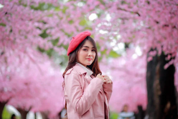 春の日には公園内のピンク色に満開の桜の美しい赤い帽子と滑らかな革のドレスを着た旅行者のヒップスター女性観光客 — ストック写真