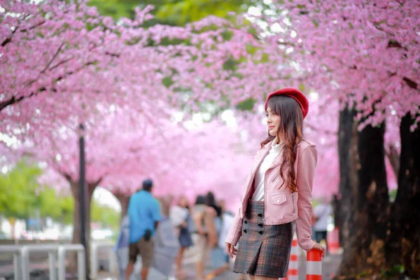 春の日には公園内のピンク色に満開の桜の美しい赤い帽子と滑らかな革のドレスを着た旅行者のヒップスター女性観光客 — ストック写真