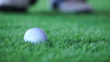 Çimlerde ve erkek ayaklarında golf topu ve golf sopası görüntüleri topa vuracak.