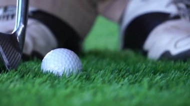 Çimlerde ve erkek ayaklarında golf topu ve golf sopası görüntüleri topa vuracak.