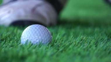 Çimlerde ve erkek ayaklarında golf topu ve golf sopası görüntüleri topa vuracak.