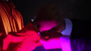 4K görüntülerinde üniformalı mahkum ve polis arka plandaki renkli ışıklarla kelepçelerini çıkarıyor. 