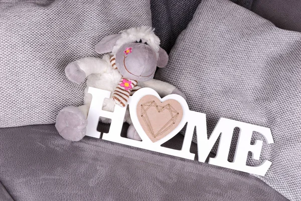 The word Home in white letters and toys sheep on a sofa