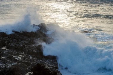 Güçlü dalga deniz kenarı lav kayaları günbatımında karşılamaktadır.