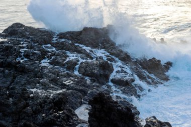 Güçlü dalga deniz kenarı lav kayaları günbatımında karşılamaktadır.