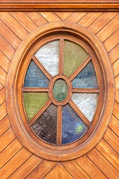 Oval window with colorful glass panes in a wooden wall