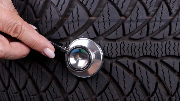 Hand of woman with stethoscope on the profile of the tire. Auto repair concept