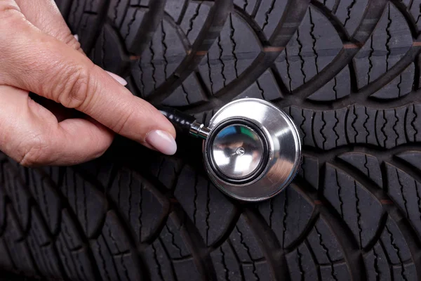 Hand of woman with stethoscope on the profile of the tire. Auto repair concept