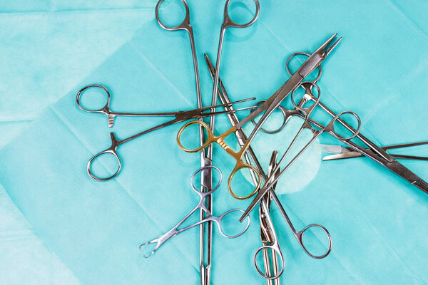 Хаос на операционном столе. Хирургические ножницы и зажимы на зеленой марле. Медицинские инструменты
