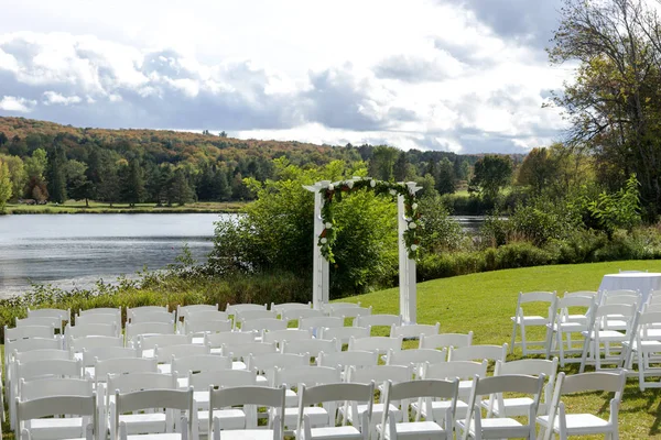 Place for wedding ceremony at the Lakeshore. Wedding arch decorated with flowers and white chairs on each side of archway outdoors