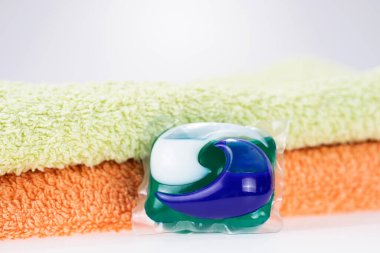 İki havlunun önünde bir kapsülde üç tane çamaşır deterjanı.