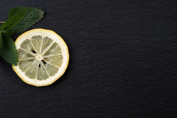 Top view of sliced yellow lemon with leaves of fresh lemon balm (Melissa officinalis) on black background