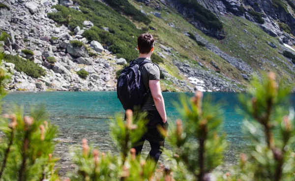 Dağ gezisine çıkmış bir adam dağlara bakıyor. Görünür dağlar ve dağ gölü.