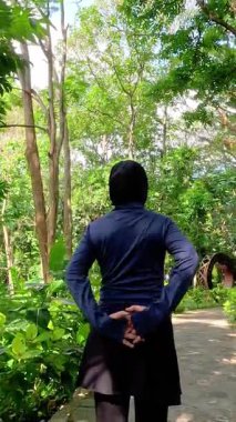 Parkta egzersiz yaparken esneme hareketleri yapan bir kadın. Yoga ve fitness antrenmanlarından önce kadın egzersizi. Spor giyim sektöründe Müslüman bir kadın.