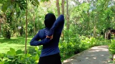 Parkta egzersiz yaparken esneme hareketleri yapan bir kadın. Yoga ve fitness antrenmanlarından önce kadın egzersizi. Spor giyim sektöründe Müslüman bir kadın.