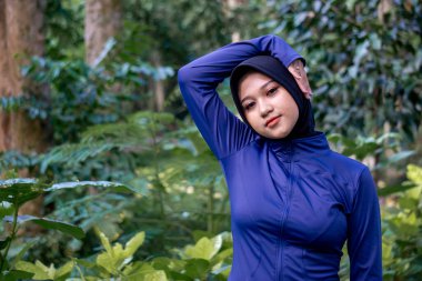 Parkta egzersiz yaparken esneme hareketleri yapan bir kadın. Yoga ve fitness antrenmanlarından önce kadın egzersizi. Spor giyim sektöründe Müslüman bir kadın.