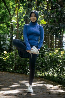 Parkta egzersiz yaparken esneme hareketleri yapan bir kadın. Yoga ve fitness antrenmanlarından önce kadın egzersizi. Spor giyim sektöründe Müslüman bir kadın.